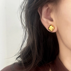 Minimalist polished gold four-leaf clover stud earring shown on a female ear