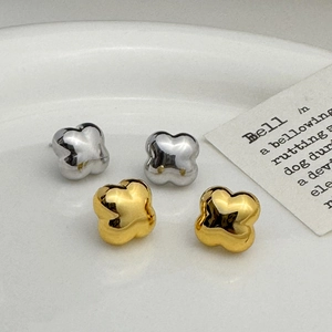 Minimalist clover flower stud earrings in polished gold and silver finishes on a tray