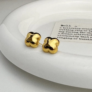 Close-up of gold flower stud earrings on a white ceramic plate with aesthetic paper