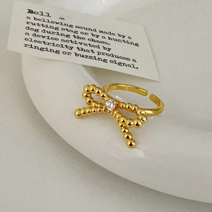 Golden beaded bow ring with sparkling zircon center on a minimalist ceramic plate