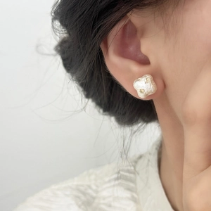 Détail des boucles d'oreilles trèfle crème avec pétales texturés et centre doré