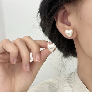 Gros plan de boucles d'oreilles cœur crème texturées portées par un mannequin