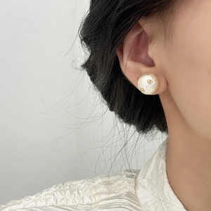 Gros plan d'une boucle d'oreille en perle de coton blanche avec détails en feuilles d'or