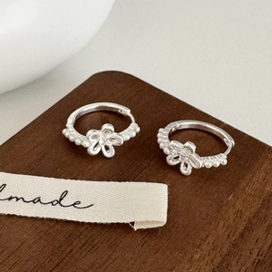 Detailed close-up of silver hollow floral hoop earrings with bead accents on wood