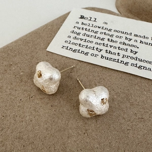 Détail de boucles d'oreilles perles blanches irrégulières avec touches dorées sur fond brun