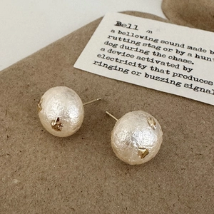 Détail de boucles d'oreilles boules texturées blanches avec accents dorés sur papier vintage