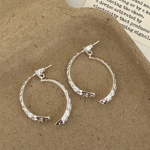 Close-up of silver C-shaped earrings with hammered texture on vintage paper background