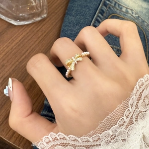 Elegant gold bow ring with sparkling crystals and white pearls worn by a model