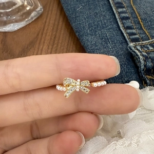 Macro detail of gold bow ring with sparkling zircons and delicate pearls on finger