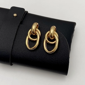 Detail of interlocking golden oval earrings placed on a premium black leather texture case