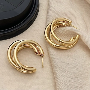 Elegant triple-layered gold hoop earrings with polished metal finish on beige fabric