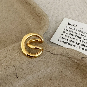 Detail of polished gold double-layered ear cuff on a minimalist texture background
