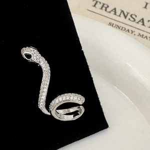 Détail macro d'un earcuff serpent argenté avec zircone blanche et yeux en pierre verte