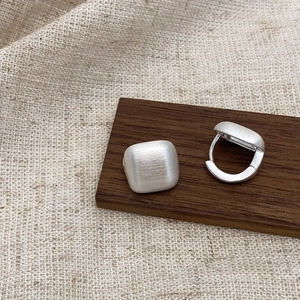 Minimalist brushed silver huggie hoop earrings displayed on a rustic wooden stand