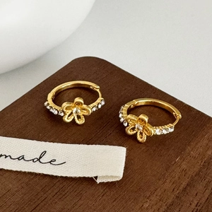 Close-up of golden flower hoop earrings with sparkling rhinestones on a wooden stand