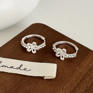 Detail of silver flower earrings with zircon pavé and brushed metal texture on wood