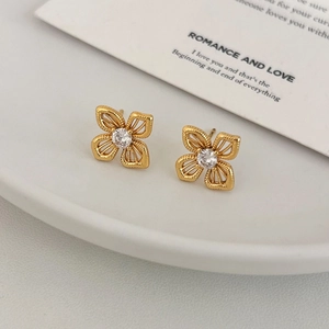 Elegant gold hollow flower stud earrings with central zircon on a minimalist white plate