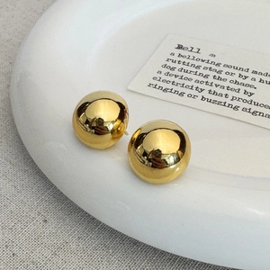 Detail view of gold mirror-finish sphere stud earrings on white ceramic plate