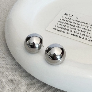 Detailed close-up of shiny silver spherical earrings on a white aesthetic ceramic tray
