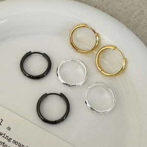 Boucles d'oreilles créoles texturées en or, argent et noir sur plateau en céramique