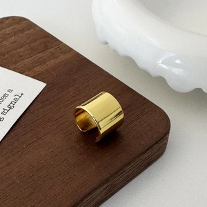 Close-up of a wide polished gold ear cuff on a dark wood background with ceramic decor