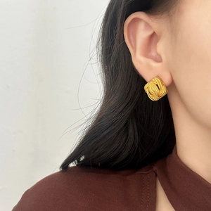 Elegant gold square stud earrings with intricate woven texture shown on a model