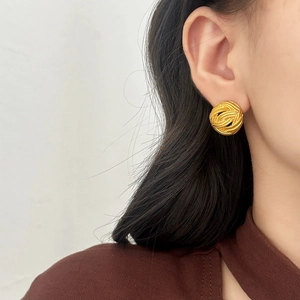 Detail view of a round vintage woven texture gold stud earring worn on a model's ear