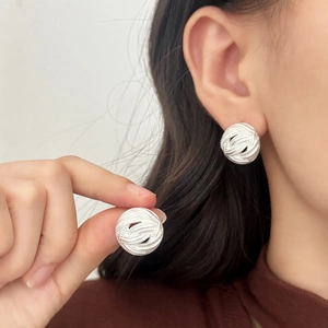 Elegant silver matte stud earrings with textured woven design worn on a female ear model