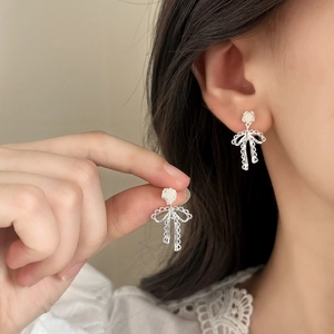Elegant silver lace bow earrings with white floral pearls worn by a model