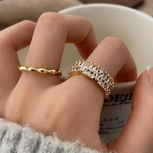 Gold wavy line ring and stacked sparkling zircon band set worn on hand holding a white cup