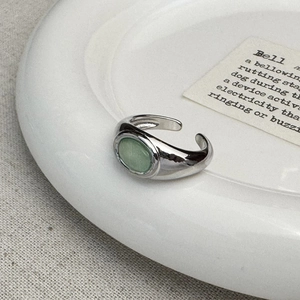 Detailed view of silver open ring with oval green opal on a minimalist white ceramic plate