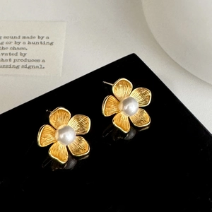 Close-up of golden flower stud earrings with pearl center and brushed metal texture