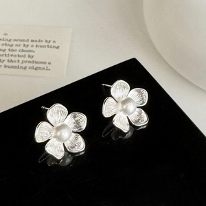 Macro detail of silver flower stud earrings with a pearl center on a reflective surface