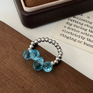 Detail of beaded silver ring featuring four faceted light blue glass gems on wood