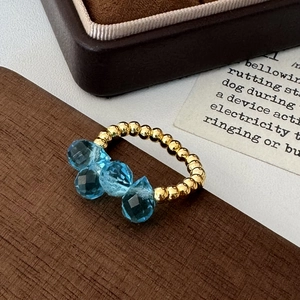 Detail of beaded gold ring with four faceted blue crystals on rustic wooden background