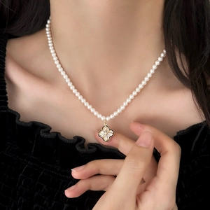 Elegant pearl necklace set with a golden four-leaf flower pendant on a model