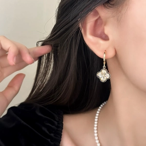 Detail of four-leaf clover drop earrings with white shell inlay and gold finish on model