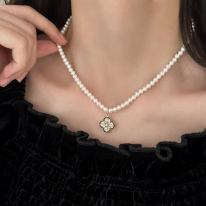 Detail view of a pearl necklace with a black enamel clover pendant worn by a model