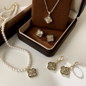Detailed set of gold clover jewelry with pearls and stones in a brown velvet gift box