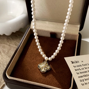 Close-up of pearl necklace with gold four-leaf clover pendant in a velvet box