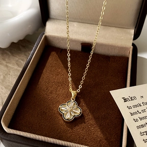 Detailed close-up of gold clover necklace with black enamel and zircons in a jewelry box