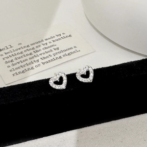 Detailed close-up of hollow heart stud earrings with cubic zirconia on black velvet