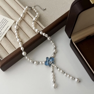Détail du collier en Y avec pendentif fleur émaillée bleue et perles sur velours doux