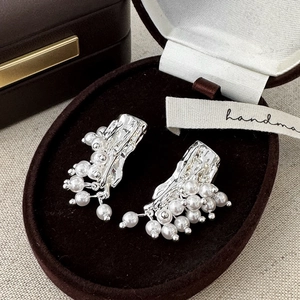 Detailed view of silver wrinkled metal earrings with white pearls on brown velvet tray