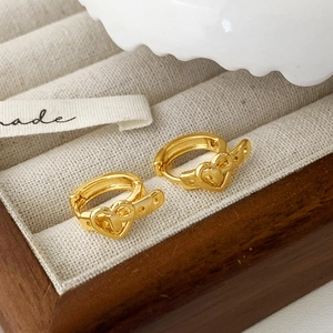 Golden heart-shaped belt-style buckle earrings displayed on a white jewelry cushion