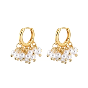 Élégantes boucles d'oreilles créoles dorées avec pampilles de perles blanches sur fond blanc