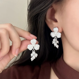 Elegant matte flower earrings with pearl tassels shown in hand and on a model's ear