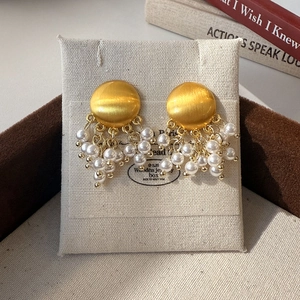 Détail de boucles d'oreilles dorées en métal brossé avec pampilles de perles blanches