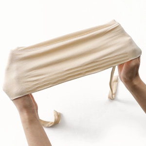 Dettaglio delle mani che allungano il materiale elastico beige del turbante a maglia