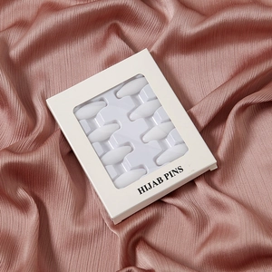 Nahaufnahme von weißen Plastik-Hijab-Nadeln in einer Sichtbox auf rosa Satin.